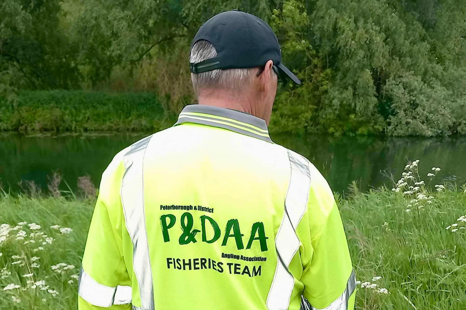 A fishery team member in hi-vis standing on the bank, looking out over a still water.