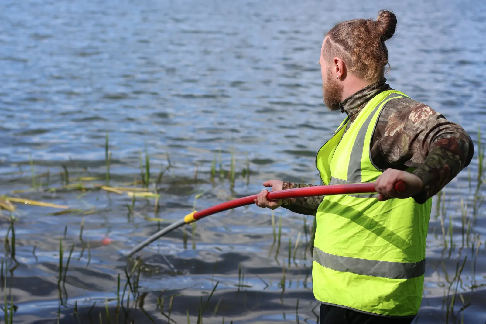 A club volunteer in a hi-vis vest working with a pole saw on bankside vegetation at a still water — one of the many forms of contributor work that keeps freshwater habitats functional. No glamour, no documentary lighting, just the work.